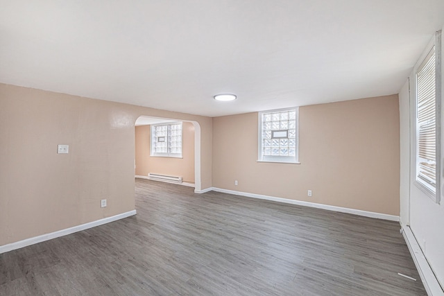 below grade area with a baseboard radiator, wood finished floors, baseboards, and arched walkways