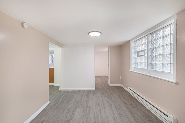 spare room featuring wood finished floors, a baseboard heating unit, and baseboards