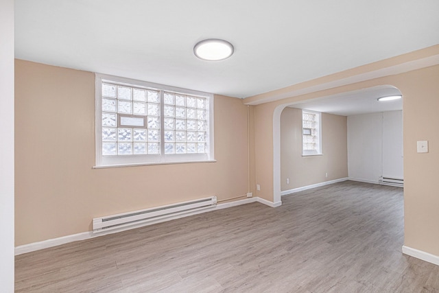 spare room featuring baseboards, arched walkways, a baseboard heating unit, and wood finished floors