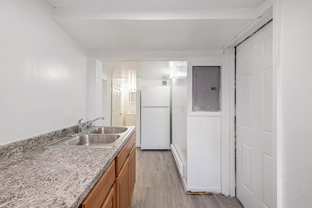 kitchen featuring freestanding refrigerator, light wood-type flooring, electric panel, a sink, and brown cabinets