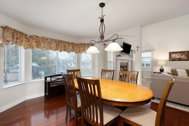 dining space with baseboards, dark wood-style floors, and a tiled fireplace