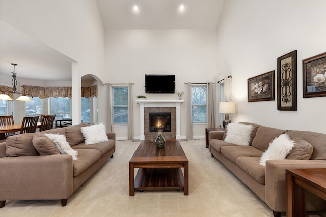 living area featuring light carpet, a high ceiling, arched walkways, and a wealth of natural light