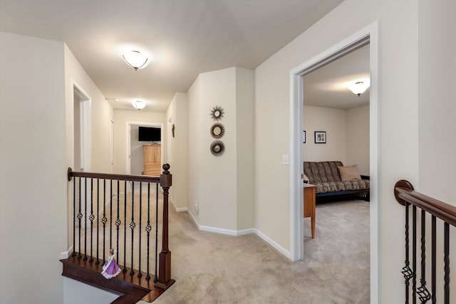 hall featuring baseboards, light carpet, and an upstairs landing