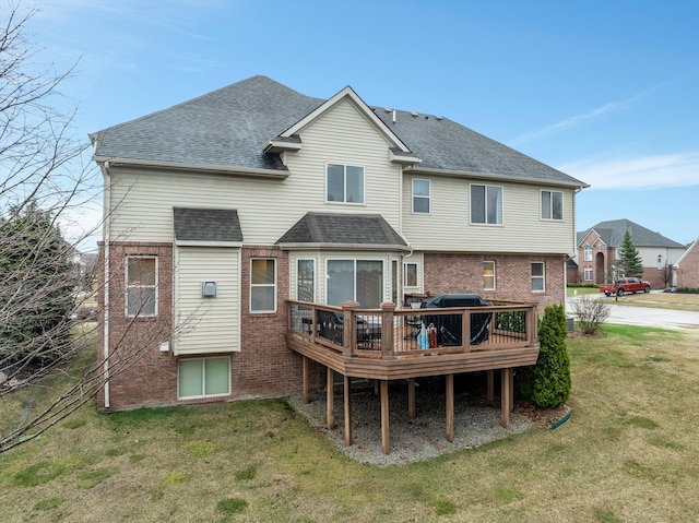 rear view of house with a shingled roof, a yard, brick siding, and a deck