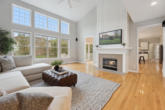 45055 Walnut Rdg, Northville, MI 48168 - living area featuring high vaulted ceiling, a ceiling fan, a tiled fireplace, light wood-style floors, and baseboards