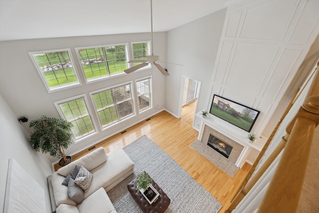 45055 Walnut Rdg, Northville, MI 48168 - living area with a tile fireplace, light wood finished floors, a ceiling fan, baseboards, and a high ceiling