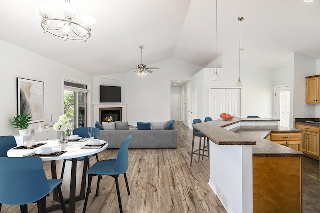 dining space with visible vents, light wood-type flooring, ceiling fan with notable chandelier, a glass covered fireplace, and vaulted ceiling