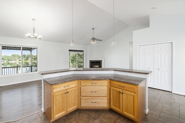 kitchen featuring a lit fireplace, dark stone countertops, ceiling fan with notable chandelier, open floor plan, and pendant lighting
