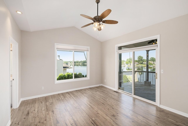empty room with ceiling fan, vaulted ceiling, a healthy amount of sunlight, and light wood finished floors