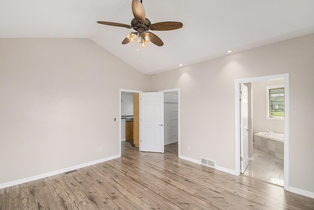 unfurnished bedroom featuring lofted ceiling, a spacious closet, baseboards, light wood-style floors, and visible vents