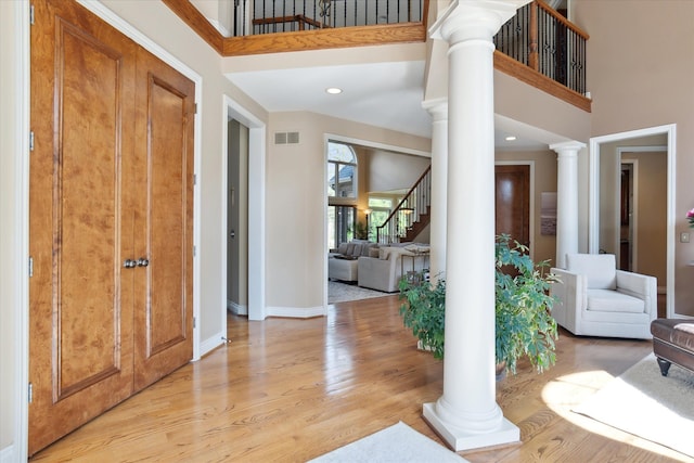 foyer entrance featuring ornate columns, a towering ceiling, visible vents, and light wood-type flooring