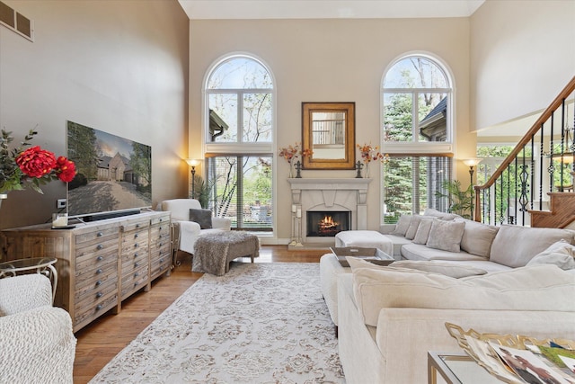 living area with visible vents, a high ceiling, a fireplace, and light wood-type flooring