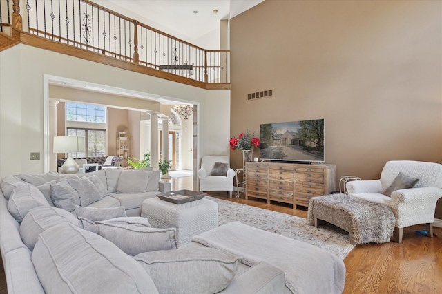 living area with decorative columns, a high ceiling, visible vents, and wood finished floors