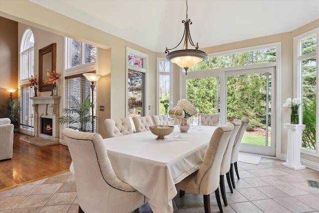 dining room with baseboards, light tile patterned floors, a warm lit fireplace, and high vaulted ceiling