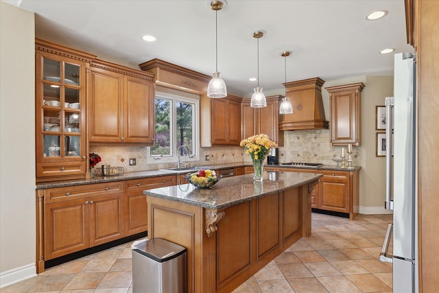 kitchen with custom range hood, a sink, baseboards, and brown cabinets