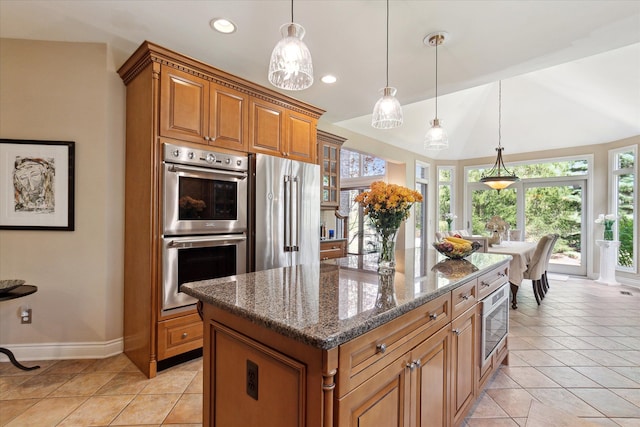 kitchen featuring dark stone counters, brown cabinets, hanging light fixtures, and stainless steel appliances