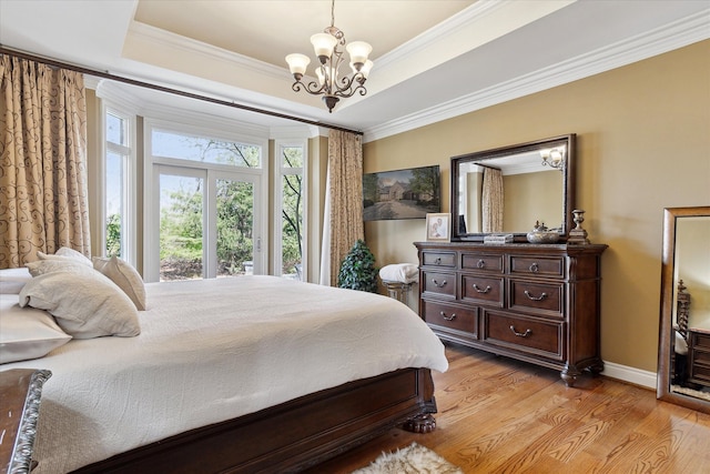 bedroom with an inviting chandelier, ornamental molding, a tray ceiling, and light wood-type flooring