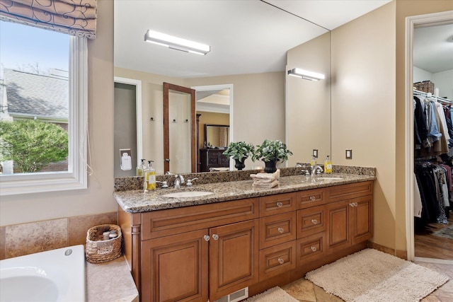 bathroom with double vanity, a walk in closet, and a sink