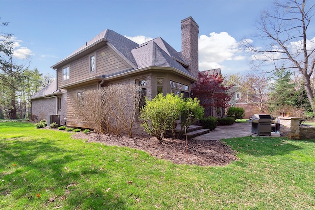 back of property with a chimney, a patio area, central air condition unit, a yard, and a shingled roof