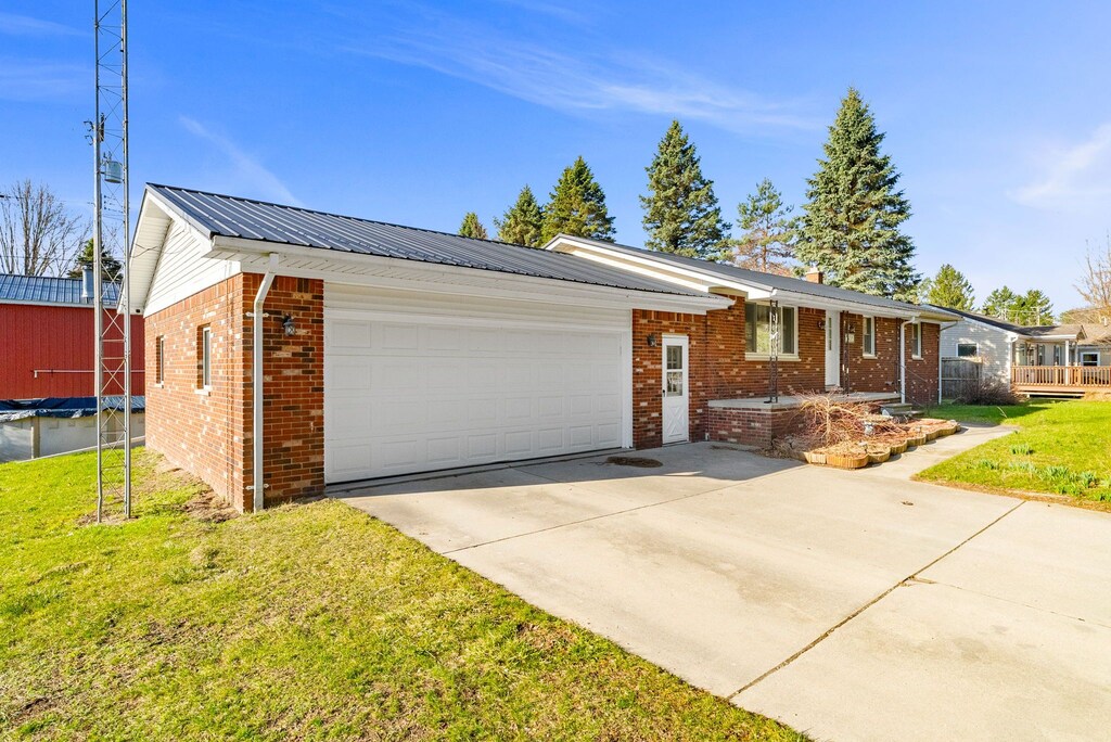 ranch-style house featuring concrete driveway, metal roof, a front lawn, brick siding, and a garage
