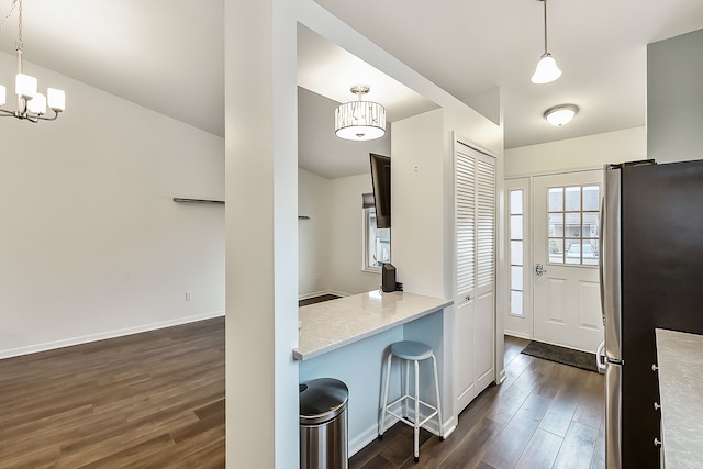 kitchen with decorative light fixtures, a notable chandelier, freestanding refrigerator, dark wood finished floors, and a breakfast bar area