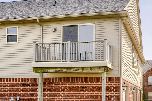 view of property exterior featuring a balcony, brick siding, and roof with shingles