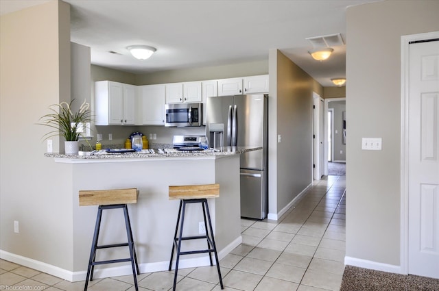 kitchen with a breakfast bar area, white cabinets, a peninsula, and appliances with stainless steel finishes