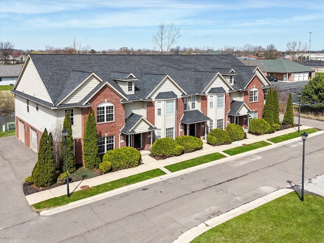 view of front of house featuring a residential view, an attached garage, brick siding, and roof with shingles