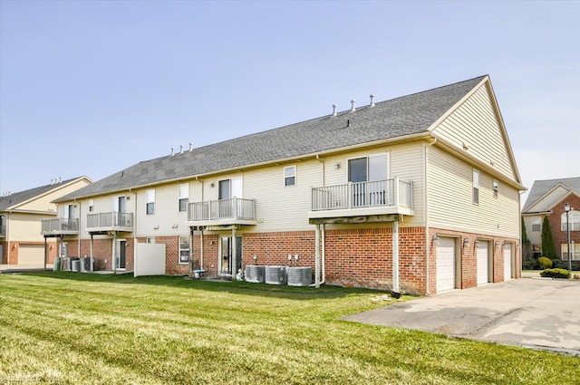 rear view of house with driveway, cooling unit, an attached garage, and a yard