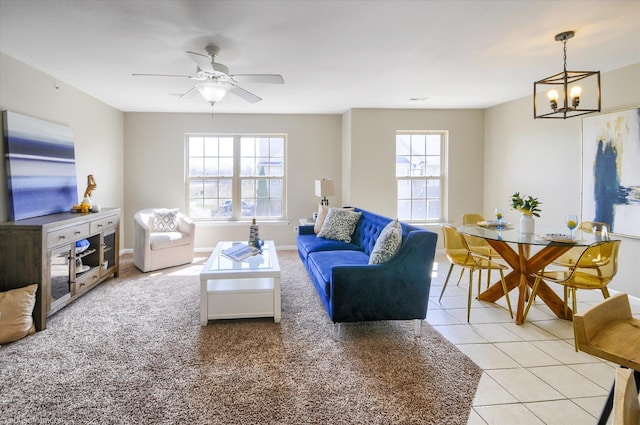 living room with light tile patterned floors, ceiling fan with notable chandelier, and baseboards