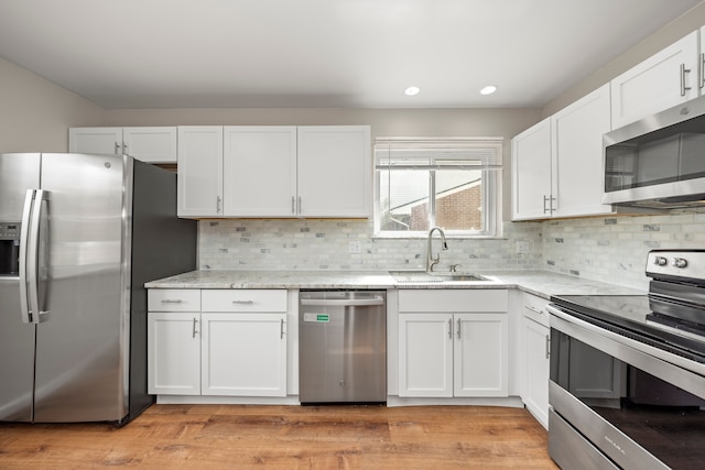 kitchen with white cabinetry, a sink, stainless steel appliances, and light stone counters