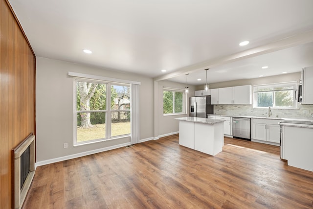 kitchen with backsplash, a sink, wood finished floors, a center island, and stainless steel appliances