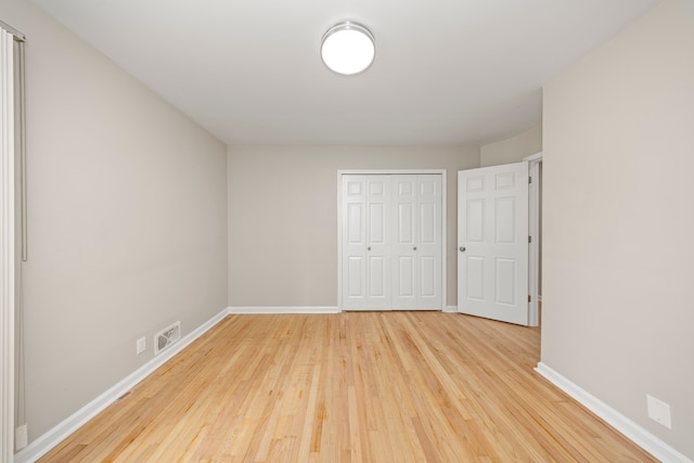 unfurnished bedroom with wood finished floors, a closet, baseboards, and visible vents