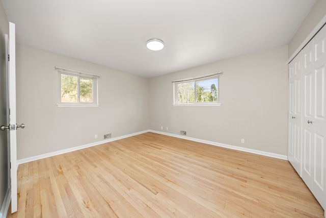unfurnished bedroom with a closet, multiple windows, and light wood-style floors