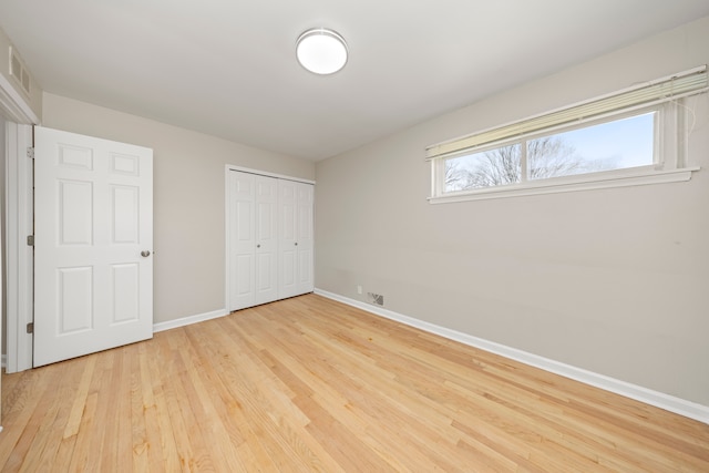 unfurnished bedroom with light wood finished floors, baseboards, visible vents, and a closet
