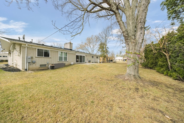 rear view of house with brick siding, a chimney, central AC unit, and a yard