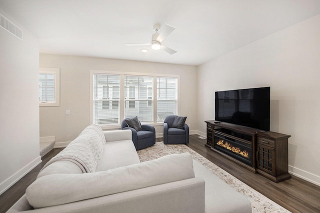 living area featuring visible vents, baseboards, ceiling fan, dark wood finished floors, and a glass covered fireplace