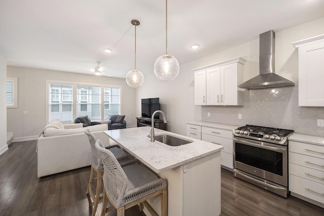 kitchen with tasteful backsplash, gas stove, a sink, open floor plan, and wall chimney range hood