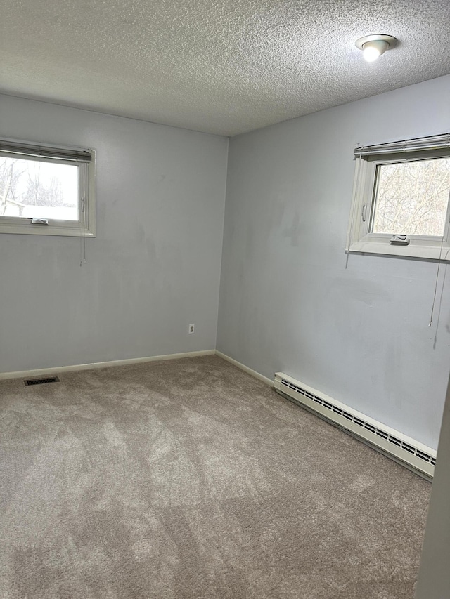 empty room with a textured ceiling, a baseboard heating unit, carpet, and visible vents