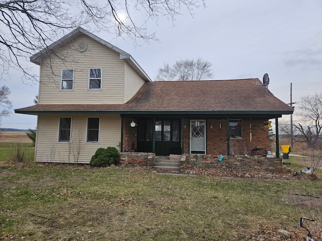traditional-style house featuring covered porch, brick siding, a front yard, and roof with shingles