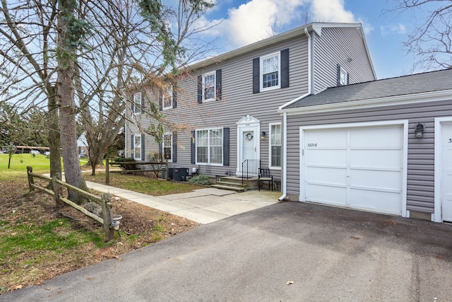 colonial inspired home featuring an attached garage, cooling unit, and aphalt driveway