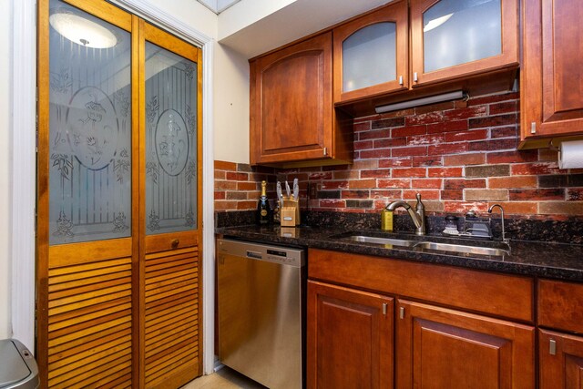 kitchen featuring dark stone countertops, glass insert cabinets, brown cabinetry, dishwasher, and a sink