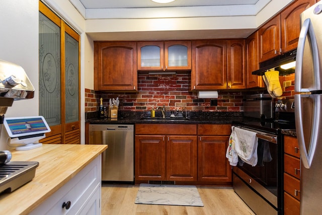 kitchen with light wood-type flooring, wooden counters, under cabinet range hood, appliances with stainless steel finishes, and a sink