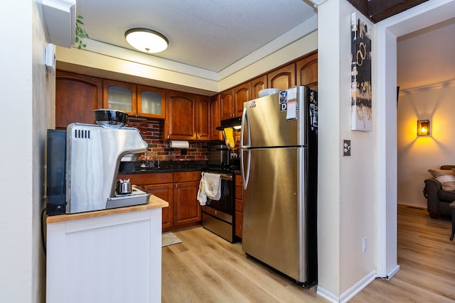 kitchen featuring brown cabinetry, light wood-style floors, under cabinet range hood, and stainless steel appliances