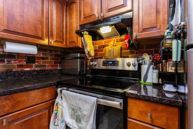 kitchen featuring dark stone counters, brown cabinetry, electric range, under cabinet range hood, and decorative backsplash