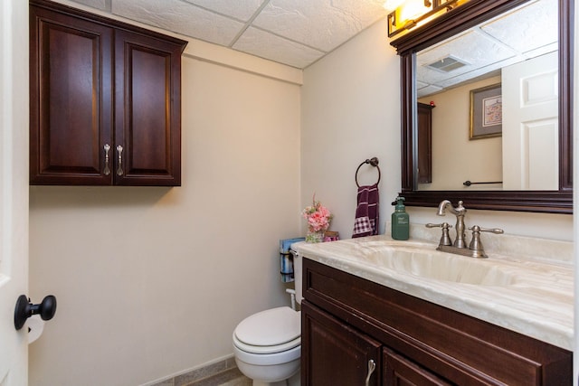 half bathroom with toilet, a paneled ceiling, vanity, and visible vents