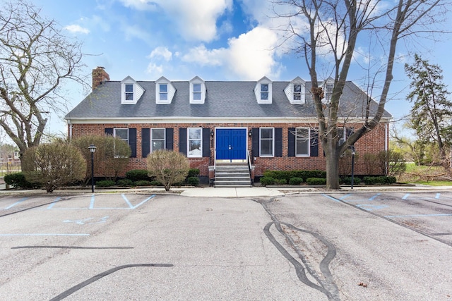 cape cod-style house featuring brick siding, uncovered parking, and a chimney