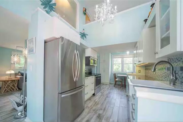 kitchen featuring backsplash, a chandelier, appliances with stainless steel finishes, light wood-style flooring, and white cabinets