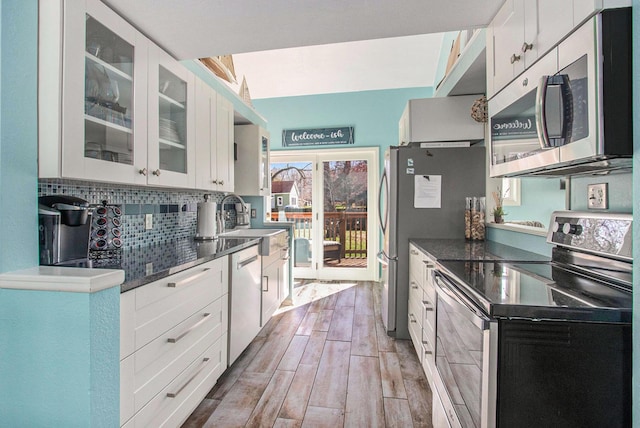 kitchen featuring stainless steel appliances, tasteful backsplash, white cabinetry, wood tiled floor, and a sink