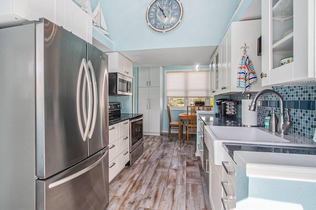 kitchen featuring backsplash, light wood-style floors, white cabinets, appliances with stainless steel finishes, and glass insert cabinets